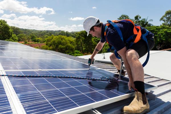 Solar panel technician with drill installing solar panels on roof on a sunny day