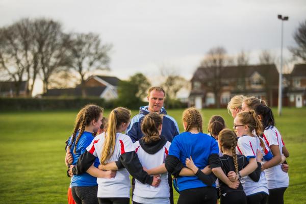 A group of teen girls and their coach in a huddle, discussing tactics